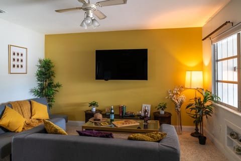Living Area & Smart TV: Gather for cozy movie nights in this vibrant living room, featuring a large wall-mounted smart TV, plush sectional sofa seating, warm floor lamps, and a central coffee table perfect for board games.