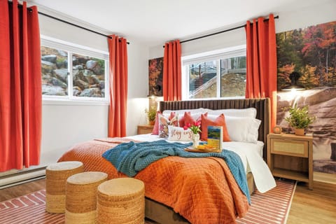 The primary bedroom with terracotta bedding, bold fall foliage murals, and two woven ottomans at the foot of the bed.