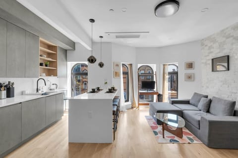 Modern open-plan studio with gray kitchen cabinetry, a white island, and large arched windows.