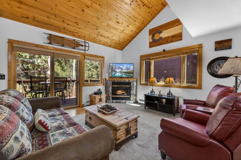 Unwind in your mountain retreat's cozy living room with vaulted wood ceilings, crackling fireplace, and panoramic forest views from your private deck.