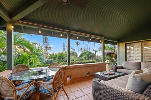 Private covered lanai with outdoor dining and lounge seating amid tropical greenery.