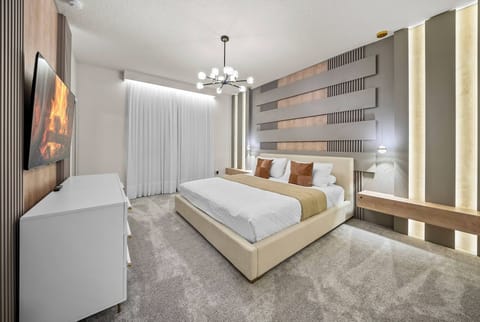 This beautifully designed bedroom offers comfort and style with a plush king-sized bed, warm textured pillows, soothing neutral tones, elegant lighting, and a sleek dresser that adds a touch of sophistication.