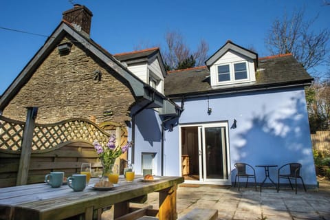Wooden outdoor table with breakfast items on a stone patio beside a cottage