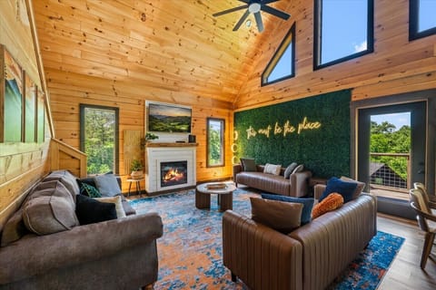 Gather around the fireplace in the spacious great room featuring comfortable seating, soaring ceilings, and a unique accent wall with custom lighting.