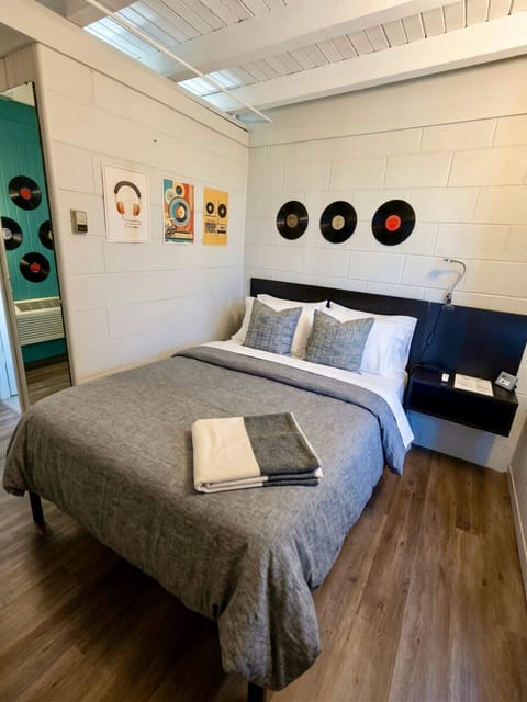 The Vinyl Lounge bedroom featuring a queen bed with plush gray bedding, blue accent pillows, and vintage vinyl records displayed above the headboard alongside retro music art prints