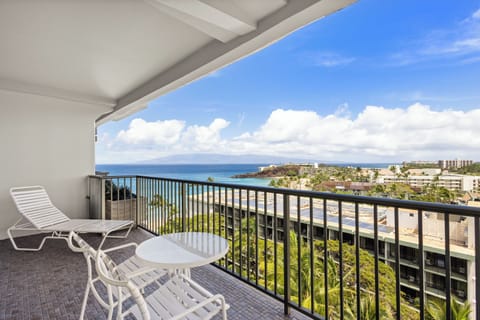 Panoramic ocean views from a covered balcony with outdoor seating overlooking tropical coastline and resort buildings.