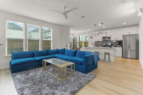 A bright open concept living room featuring a large sectional sofa, Smart TV, and oversized windows that fill the space with natural light.