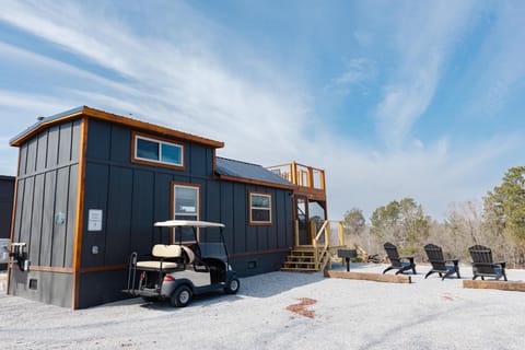 Dark gray cottage exterior with natural wood trim, a golf cart parked outside, and black Adirondack chairs on gravel.