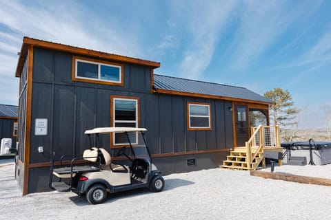 Dark gray cottage exterior with natural wood trim, small wooden steps, and a golf cart parked on gravel.