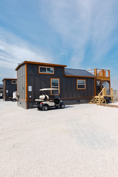 Exterior view of dark gray wood-paneled cottage with natural wood trim, metal roof, and a beige golf cart parked outside.