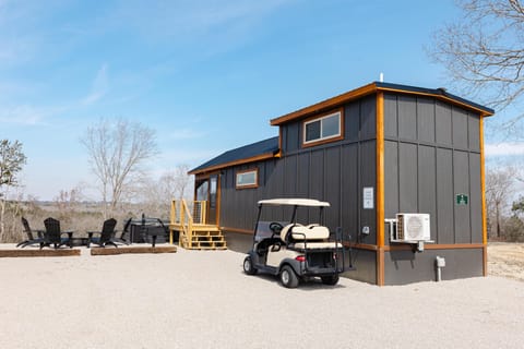 Dark gray exterior with natural wood trim, gravel driveway, golf cart, and outdoor fire pit seating area.