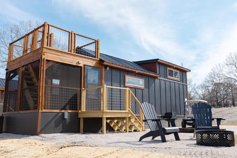 Fire pit area with two black Adirondack chairs on gravel beside screened porch and rooftop deck.