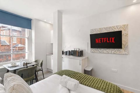 A bright, modern bedroom with a luxurious double bed, dining space for two and Smart TV with Netflix. Large windows fill the room with natural light, creating a stylish and comfortable retreat perfect for relaxing or enjoying meals in.