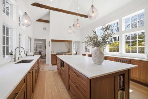 The kitchen island seats four beneath original timber beams that have been here for centuries — the wall of windows keeps the whole space bright and open.