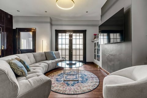 Plush sectional facing the French doors, glass coffee table, game cabinet, and swivel chair — a room made for settling in.