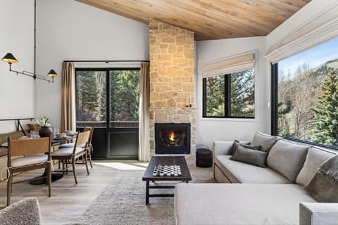 Sun-drenched living room featuring a stone fireplace and vaulted wood ceilings.