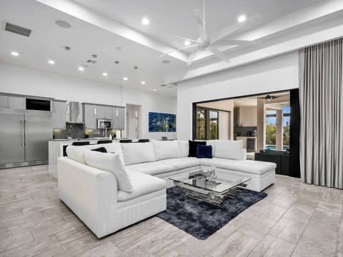 Spacious great room with comfortable lounge seating, high ceilings, a modern kitchen, and easy access to the outdoor living area.