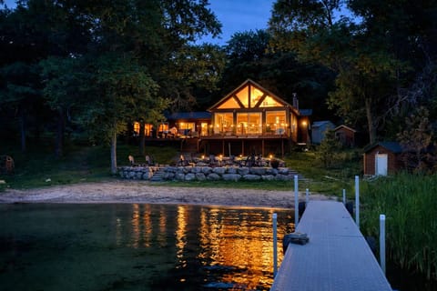 Warm, glowing cabin at night with twinkling string lights, cozy interior light, and a beautiful sandy beach. A magical lakeside setting perfect for relaxing, gathering, and making unforgettable memories.