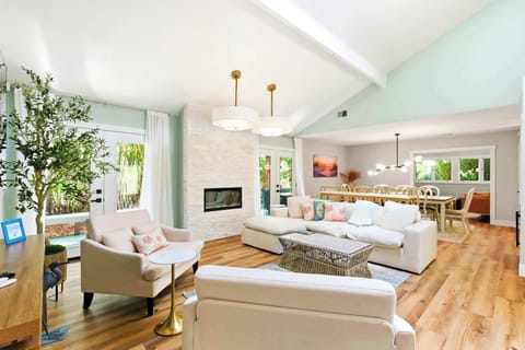 Vaulted ceilings and soft mint walls create an airy backdrop for this open living space, where a white stone fireplace anchors the room. Natural wood floors glow under the gentle afternoon light, inviting you to settle into the plush seating.