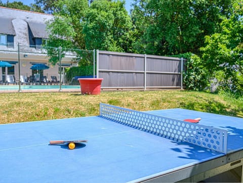 Blue outdoor ping pong table set up beside the pool — paddles and ball at the ready