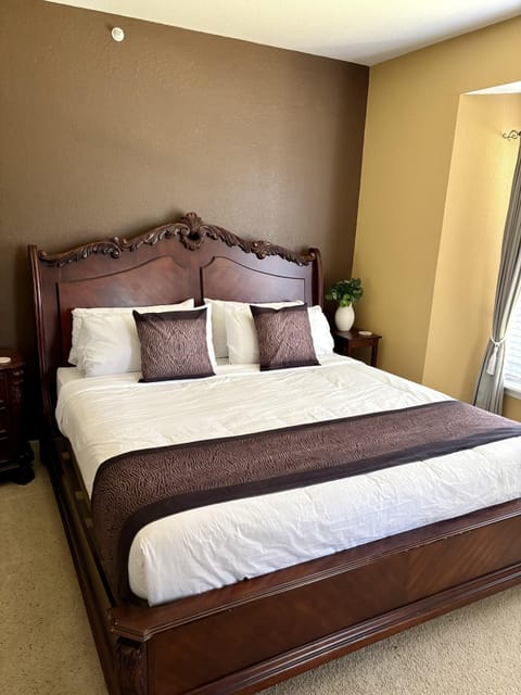 Master bedroom with carved wood bed frame, white linens, brown accent runner, and two matching pillows.