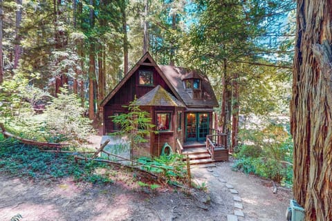 Tucked beneath towering Cazadero redwoods, your storybook cottage awaits — whimsical A-frame charm, warm wood siding, and a stone pathway leading to your private forest hideaway.
