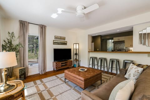 An open-concept living area featuring comfortable sofa seating, a large tufted leather ottoman, and a convenient breakfast bar looking into the fully equipped kitchen.