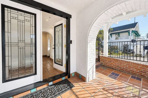 Spanish-style tiled entrance with decorative arched porch, stained glass door, and wrought-iron accents. Neighboring homes visible beyond the quiet street, marking your arrival to this charming property.