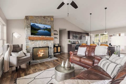 Living room with stone fireplace, smart TV, and open kitchen flow