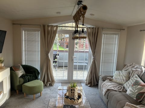 Spacious living room with recliner sofa, coffee table, seat with matching stool and smart TV. Living room also comprises of large patio doors leading onto decking area. 