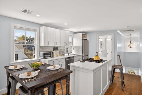 Prepare your favorite meals in this bright, fully-equipped kitchen with sleek white cabinetry, stainless steel appliances, and a convenient island with gas cooktop. Natural light pours in, making cooking a joy.