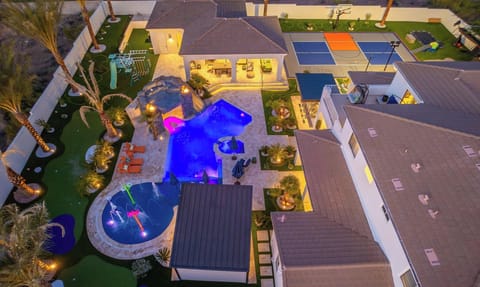 Aerial view of an impressive resort-style property featuring multiple pools, outdoor entertainment areas, and landscaped grounds illuminated for evening enjoyment.