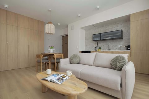 A modern living room with a light sofa, wooden accents, and an open kitchenette in the background.