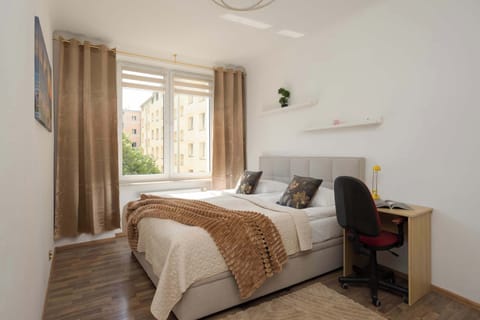 A cozy bedroom with a double bed, wooden flooring, and a desk placed near the window.