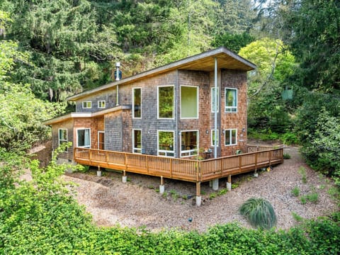 Modern retreat nestled among lush evergreens, featuring a spacious wraparound deck and floor-to-ceiling windows that invite natural light and forest views throughout.