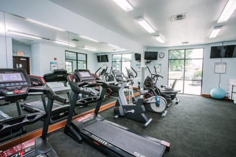 Fitness room with treadmills, ellipticals, wall-mounted TVs, and mirrored walls — open during your stay.