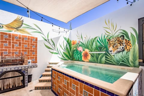 Tiled plunge pool in a sunny courtyard with a tropical jaguar mural and adjacent brick barbecue Argentinian grill.
