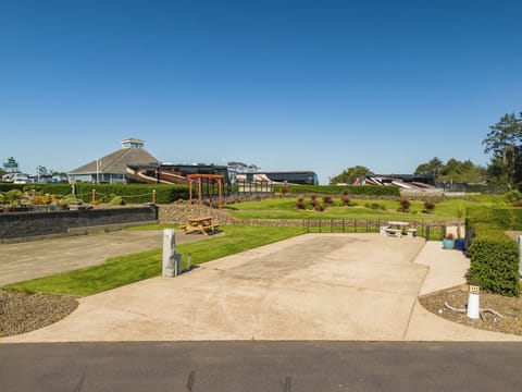 The property features a spacious lawn with picnic areas, landscaped gardens, and a pergola, all set within a well-maintained resort community under clear skies.