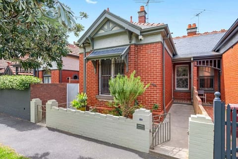 A charming red-brick cottage with ornate trim, a cozy front garden, and a narrow pathway leading to the entrance.