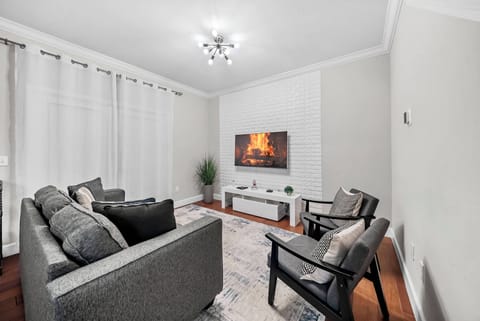 Relax in our cozy living room with a plush gray sectional and chic black accent chairs, ideal for unwinding after a day of adventure. Bright curtains and a modern fireplace create a warm, inviting atmosphere for your stay.