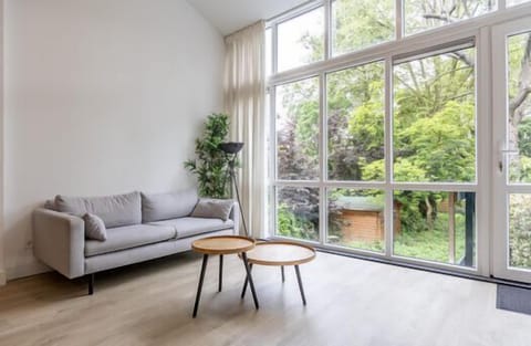 The apartment features a spacious open-plan living and dining area with large windows facing greenery, creating a bright and calm interior. The modern kitchen is fully equipped and integrated into the living space.