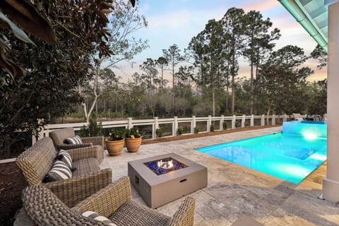 Relax on your private patio with cozy wicker seating, a modern fire pit, and a sparkling pool—all surrounded by peaceful wooded views and a stunning evening sky.