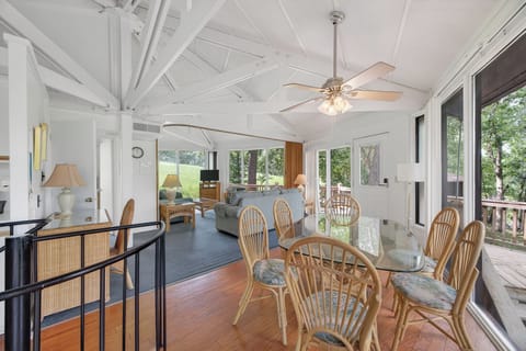 Bright, open living and dining space with soaring vaulted ceilings and panoramic windows framing lush treetop views, inviting you to gather and relax in style.