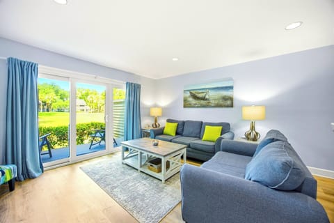 Sliding glass doors draw the afternoon brightness into this airy living room, where plush seating and lime accents meet pale wood floors. It is a cheerful spot to gather after a day exploring the lush greenery just outside the porch.