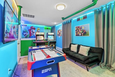 Welcome to our vibrant game room, where fun and laughter await! Enjoy a colorful air hockey table and classic arcade games surrounded by bright blue walls.