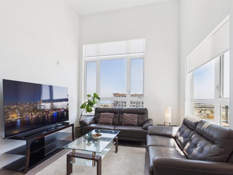 Welcome home! Relax in a bright, sun-drenched living room featuring soaring high ceilings, expansive windows, and plush leather seating.