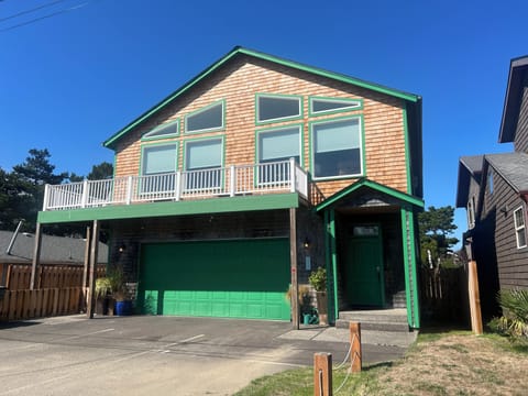 Distinctive vacation rental home featuring cedar shake siding, bright green trim, and large windows welcoming guests to a peaceful neighborhood setting.