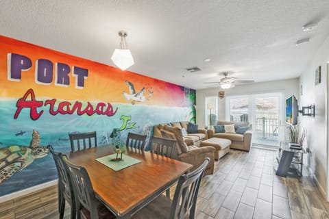 A vibrant Port Aransas mural welcomes you into a bright, open living space where you can unwind by the windows and soak in coastal charm together.