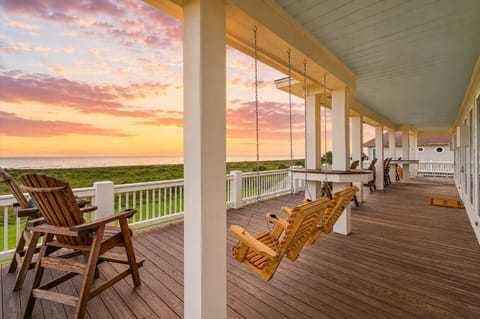 Expansive covered deck with rocking chairs, outdoor dining space, and stunning sunset views near Crystal Beach, Texas vacation rental.