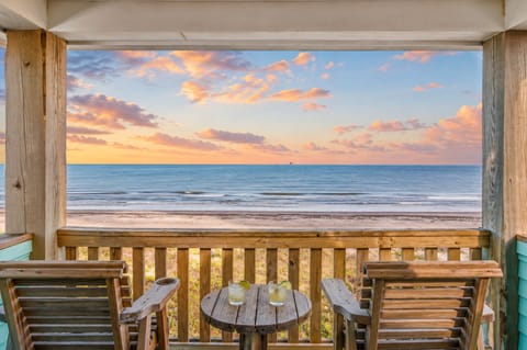 Beachfront balcony with outdoor dining, wooden lounge chairs, and panoramic Gulf views at Port Bolivar TX vacation rental perfect for sunrise coffee and relaxing coastal getaways.
